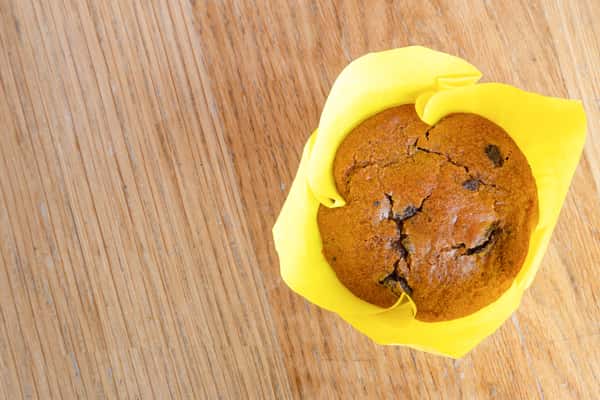 Top-down view of a freshly baked chocolate chip muffin wrapped in bakery paper and ready for grab-and-go breakfast service.