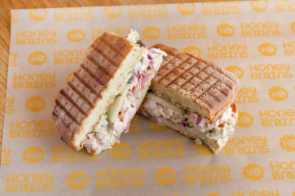 Grilled tuna salad sandwich on artisan bread with fresh greens and vegetables, served as a healthy café lunch option.