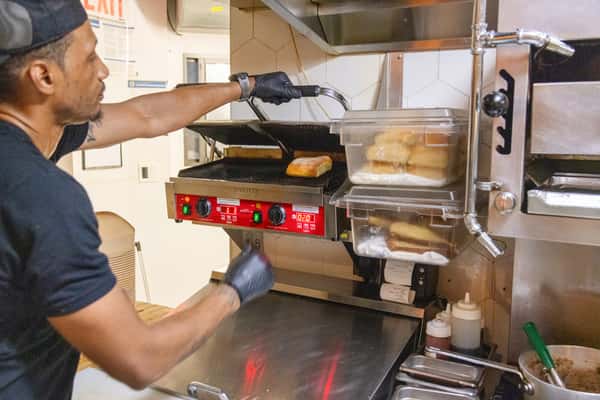 Kitchen staff pressing artisan sandwiches on a commercial grill for fresh made-to-order café service.