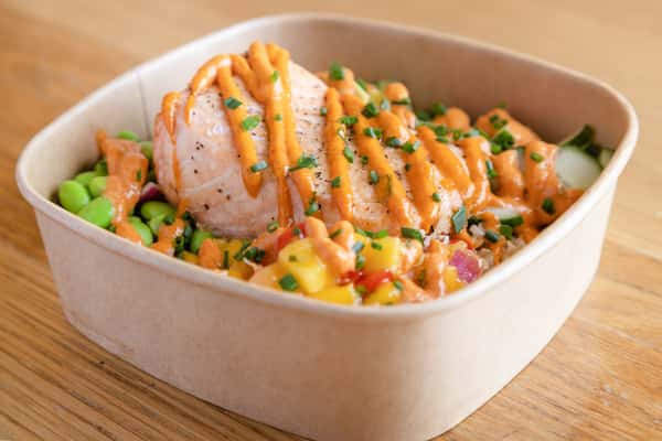 Salmon grain bowl topped with fresh vegetables, grains, and creamy sauce for a healthy, protein-packed meal.