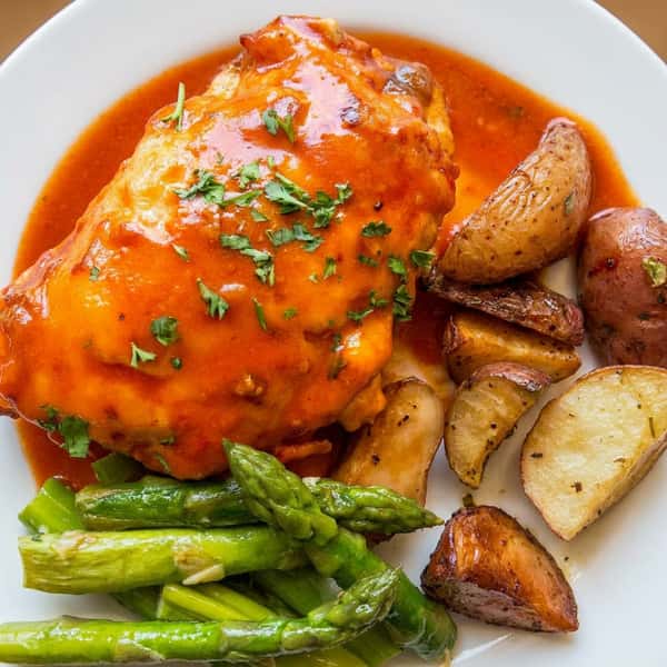 Chicken in red sauce with roasted potatoes and asparagus.