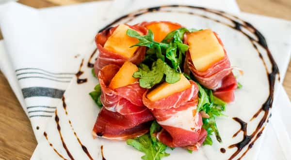 prosciutto melon arugula in a white plate