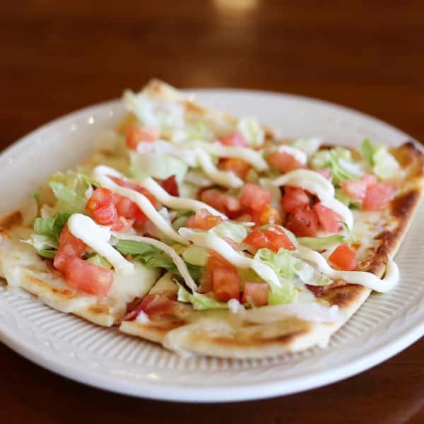 flatbread with lettuce, tomatoes and a sauce on a plate