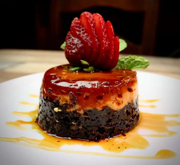 Chocoflan dessert topped with a sliced strawberry and mint leaf, drizzled with caramel sauce on a white plate.