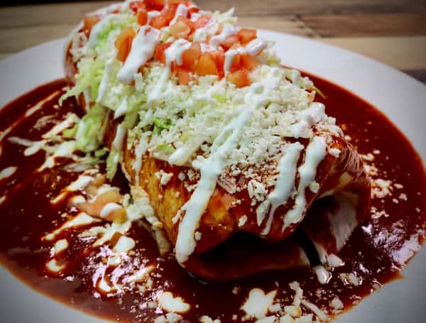 Crispy flautas topped with shredded cabbage, crema, cotija cheese, and red salsa on a white plate.