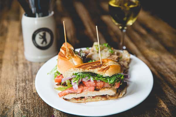 Grilled chicken sandwich topped with bacon, lettuce, tomato, and melted cheese on a toasted bun, served with crispy fries at Berliner Pub.