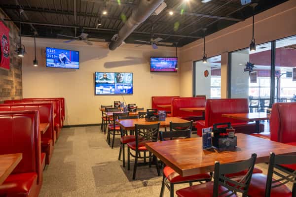 Restaurant booth seating with bright red vinyl benches and wooden tables against a wood-paneled wall, decorated with framed sports jerseys and wall-mounted lights.