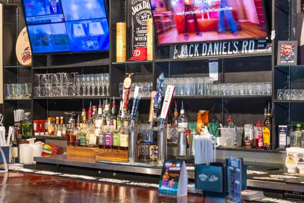 Close-up of several beer taps at a bar, including handles for lager, cider, IPA, and Michelob Ultra, with liquor bottles and glassware in the background.