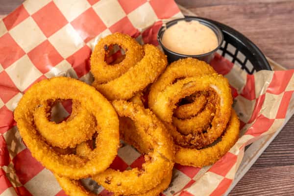 Crispy golden onion rings served in a checkered basket with a side of creamy dipping sauce.