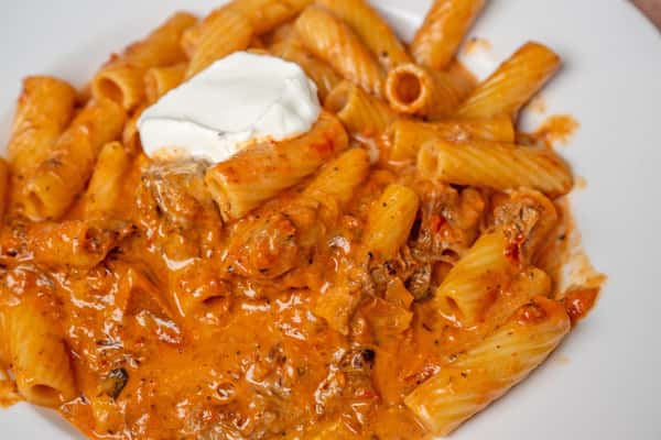 Rigatoni pasta in creamy tomato sauce with sausage, topped with a dollop of ricotta on a white plate.