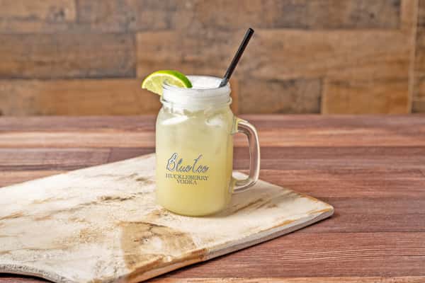 Frozen margarita in a mason jar with a lime wedge and black straw on a wooden table.