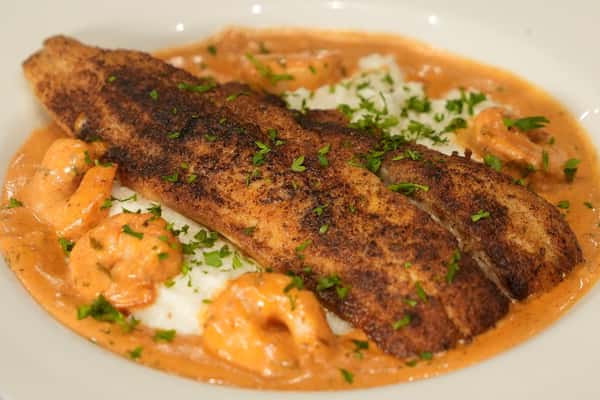 Blackened fish fillets served with shrimp in a creamy sauce over rice, garnished with fresh parsley.
