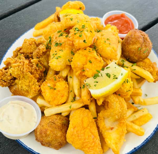 Seafood platter with fried shrimp, fish, oysters, hush puppies, and French fries, served with lemon wedge, tartar sauce, and cocktail sauce.