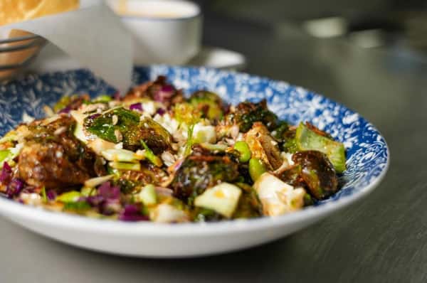 Crispy Brussels sprouts tossed with shredded cabbage, edamame, and a savory glaze, served in a blue patterned bowl.