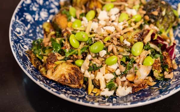 Roasted Brussels sprouts salad with edamame, sunflower seeds, kale, and crumbled cheese in a patterned blue bowl.