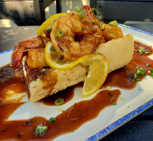 New Orleans-style BBQ shrimp served over crusty French bread, garnished with lemon slices and green onions in a rich, buttery sauce.