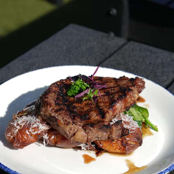 Grilled ribeye steak served over crispy smashed potatoes and wilted spinach, topped with shredded Parmesan and fresh herbs.