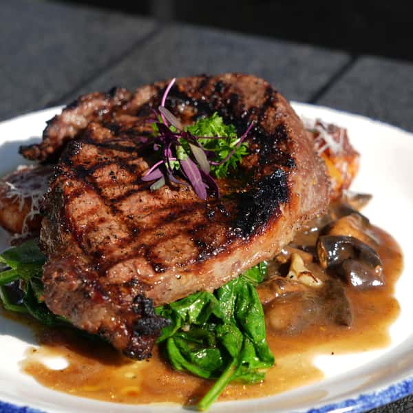 Grilled steak served over sautéed spinach with a savory mushroom sauce, garnished with fresh herbs and a sprinkle of Parmesan cheese.