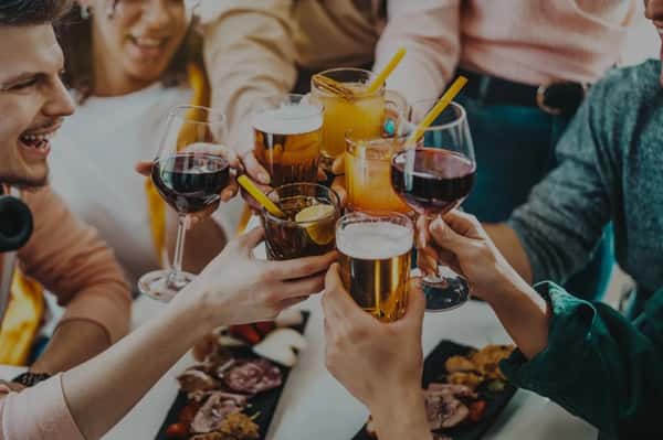 A group of people clinking glasses filled with different drinks, including wine, beer, and cocktails, celebrating together.