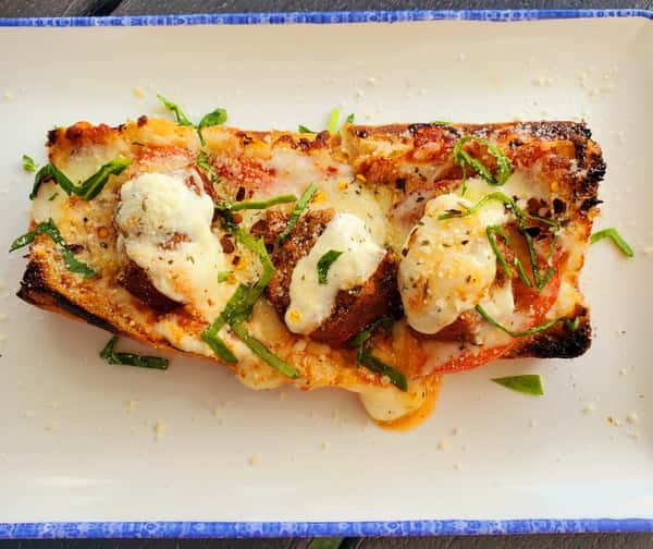 Toasted French bread pizza topped with meatballs, tomato slices, mozzarella, basil, and grated Parmesan cheese.