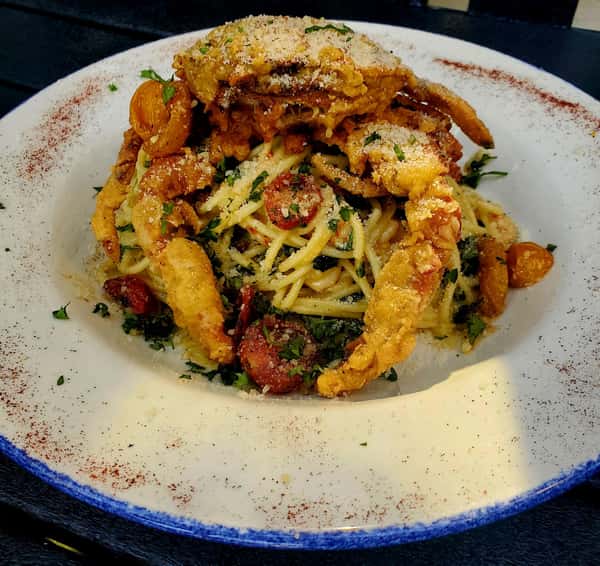 Crispy soft-shell crabs over a plate of spaghetti with herbs, cherry tomatoes, and parmesan cheese.