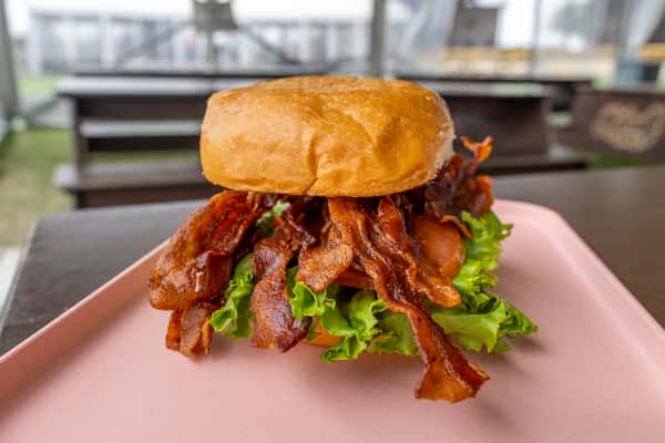 Crispy bacon burger with fresh lettuce and tomato on a toasted golden bun, served on a light pink plate.