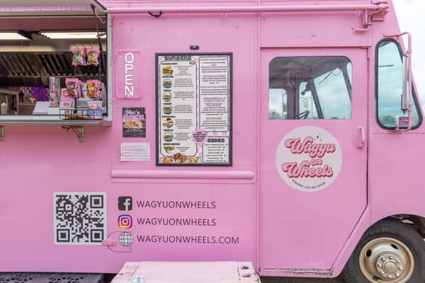 Bright pink Wagyu on Wheels food truck featuring a detailed menu, social media handles, and a retro logo.