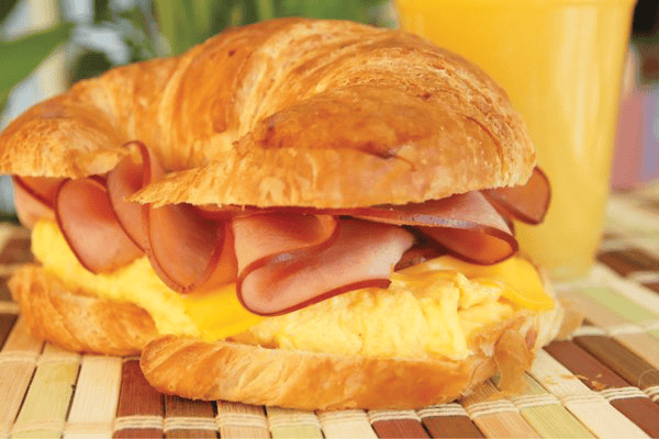 ham, eggs, and cheese on a croissant with a glass of orange juice.
