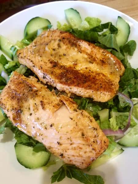 two pieces of grilled chicken over a bed of greens