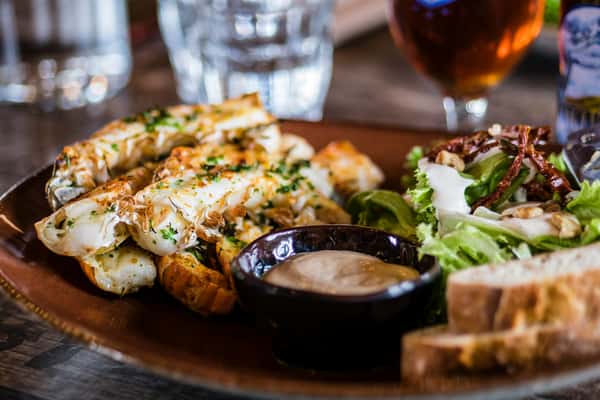 Grilled crab legs served with dipping sauce, fresh mixed greens, and slices of bread on a rustic plate.