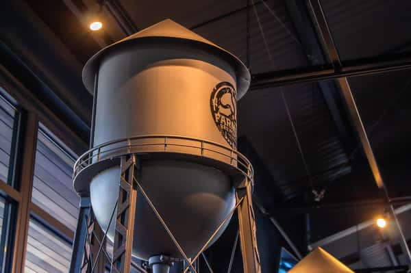 Metal water tower-style beer tap structure inside Farmers Brewing Co. taproom, featuring the brewery's logo on its side.