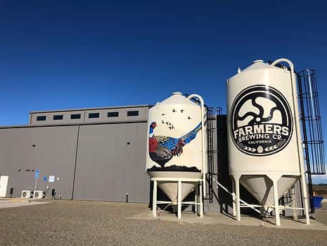 Two large silos at Farmers Brewing Co, one featuring the logo and the other painted with a colorful pheasant design