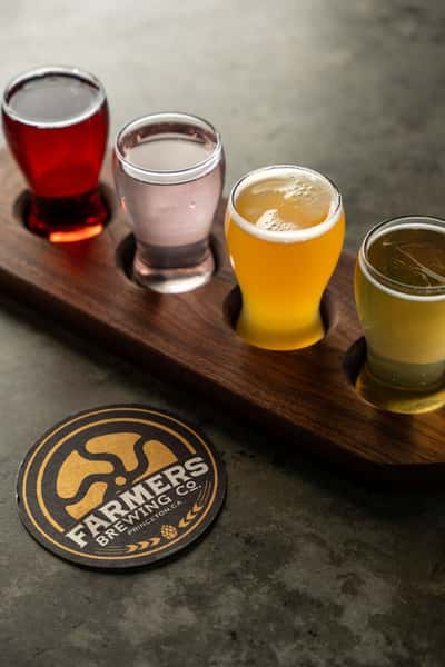 A flight of four colorful craft beers from Farmers Brewing Co. on a wooden tray with a branded coaster on the table.