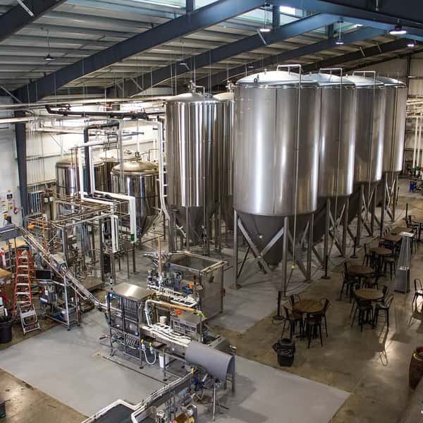 Large stainless steel fermentation tanks and brewing equipment inside a spacious brewery facility.