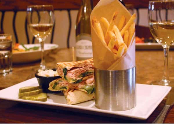 Pressed sandwich on a plate with fries and two glasses of wine