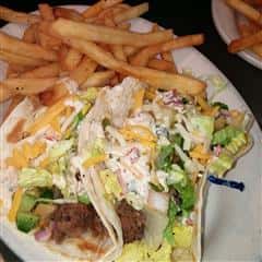 fish tacos with lettuce and cheese in a soft taco shell with a side of fries
