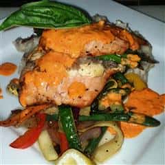 salmon menu item on a bed of grilled vegetables with orange sauce