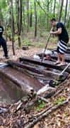 man crawling under logs in a river of water