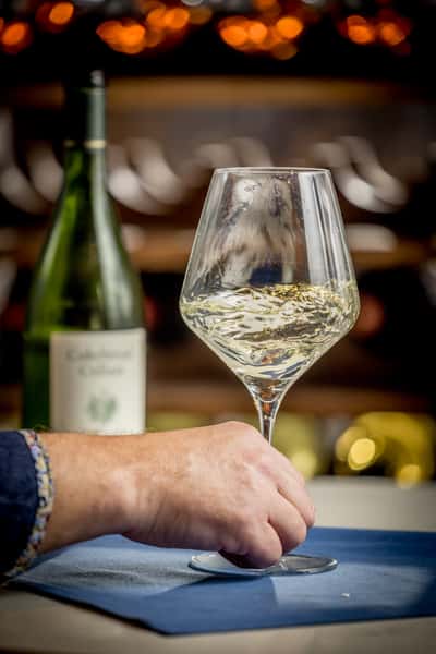 Hand holding a glass of chilled white wine with a bottle in the background at a stylish bar in St. Petersburg, FL.