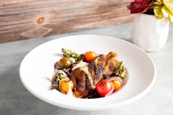 Blackened fish served with cherry tomatoes, grilled asparagus, red onions, and creamy sauce on a bed of grains in a white bowl.