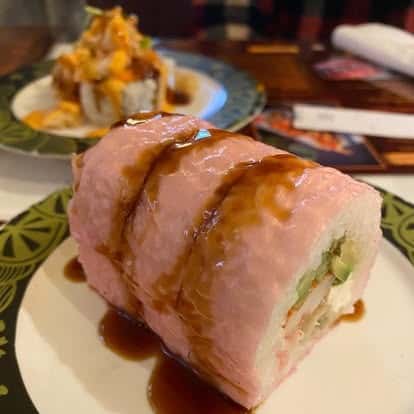 Seared tuna wrapped roll drizzled with sauce, served on a plate
