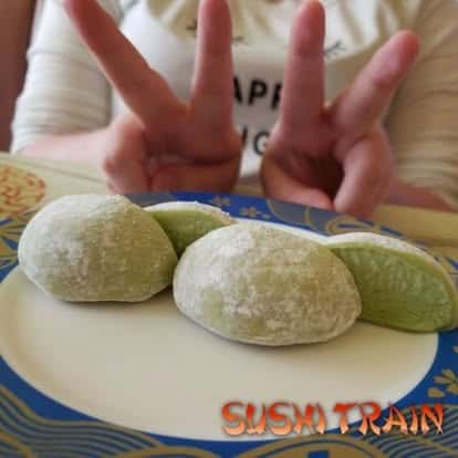 Hand holding up a peace sign next to a plate of mochi desserts