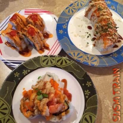 Two plates of assorted sushi rolls, one topped with orange sauce