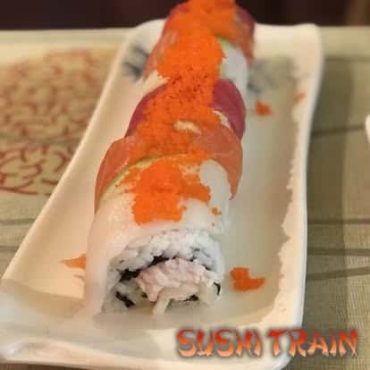 Sushi roll topped with orange tobiko and fresh fish, served on a white plate