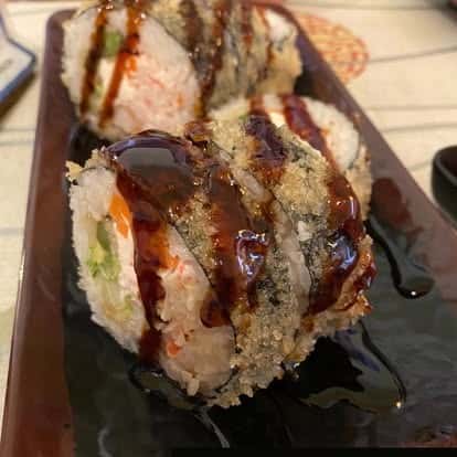 Sushi roll topped with drizzled sauce and garnish