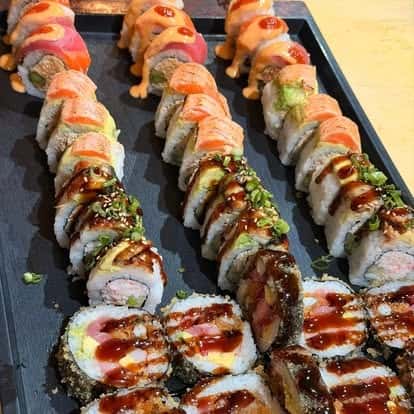 Assorted sushi rolls topped with sesame seeds and drizzled sauce, served on a black platter