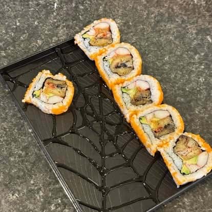 Sushi rolls topped with orange garnish, arranged in a row on a decorative plate