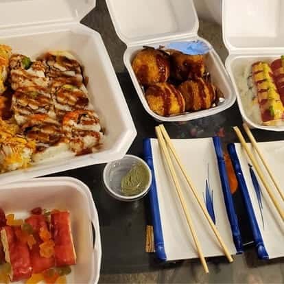 Assorted Japanese appetizers and skewers in takeout containers with dipping sauce and chopsticks