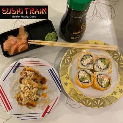 Chopsticks holding a piece of food above a plate of sushi rolls