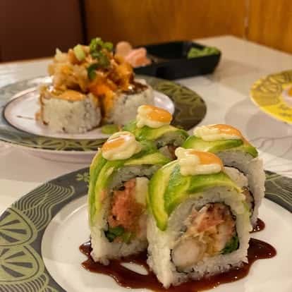 Sushi roll topped with avocado and cucumber, drizzled with eel sauce